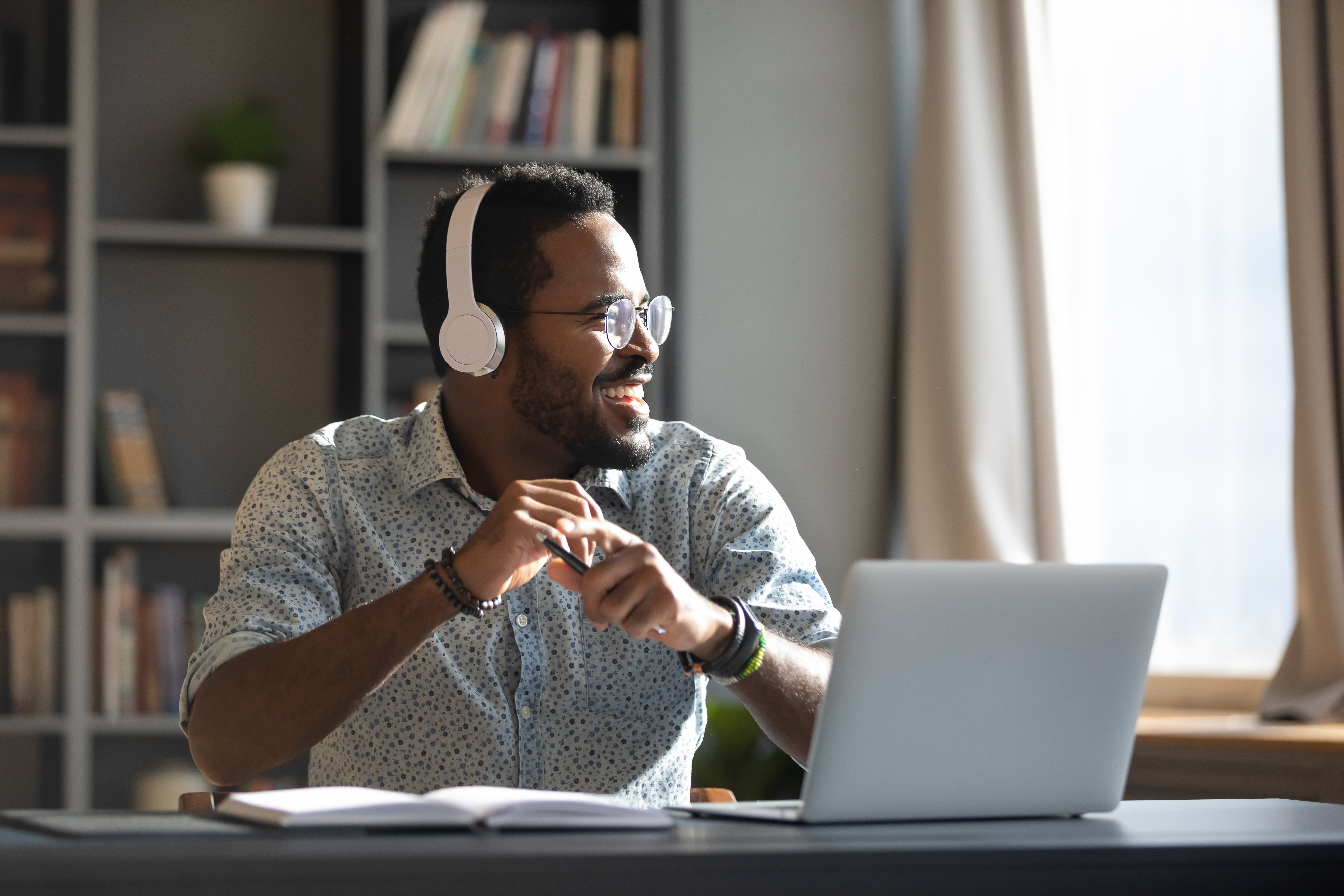 Man wearing headphones sitting on a desk with his laptop and smiling.