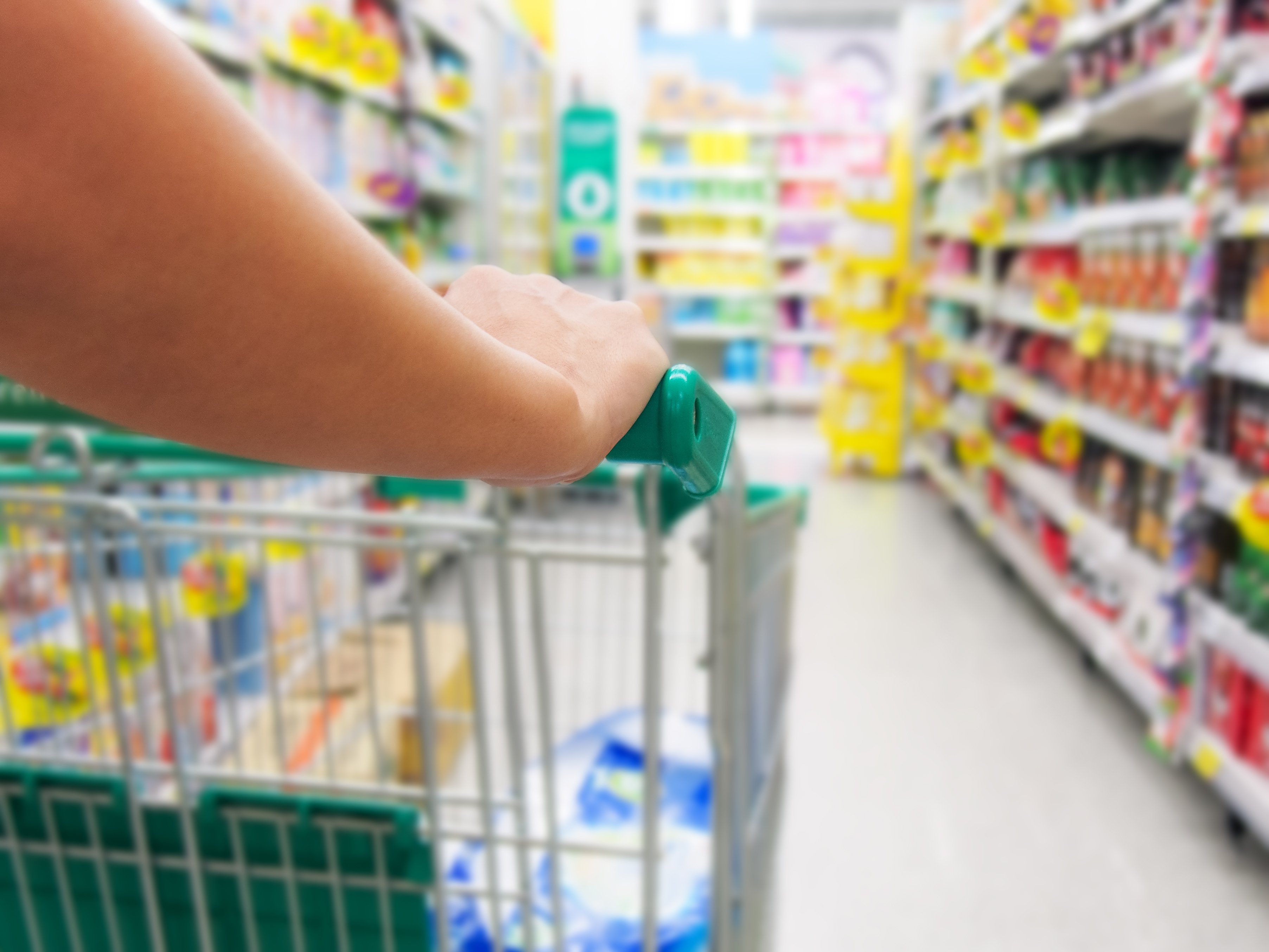 A close-up shot of someone's arm pushing a shopping trolley through a grocery aisle. Planning and sticking to a budget grocery list can help save dollars in the long-run and manage the rising costs.