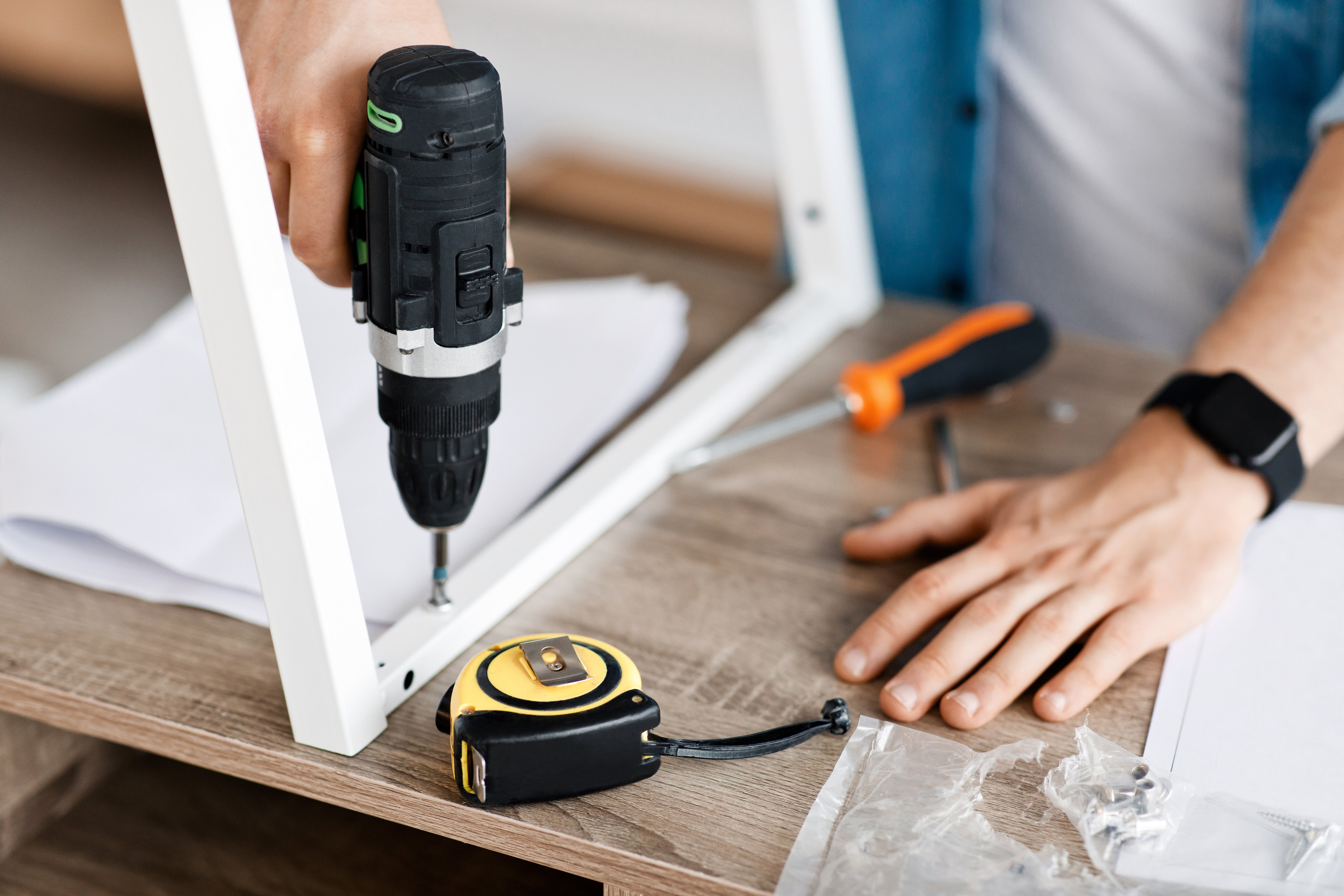 Close-up of man drilling a screw into a window frame.