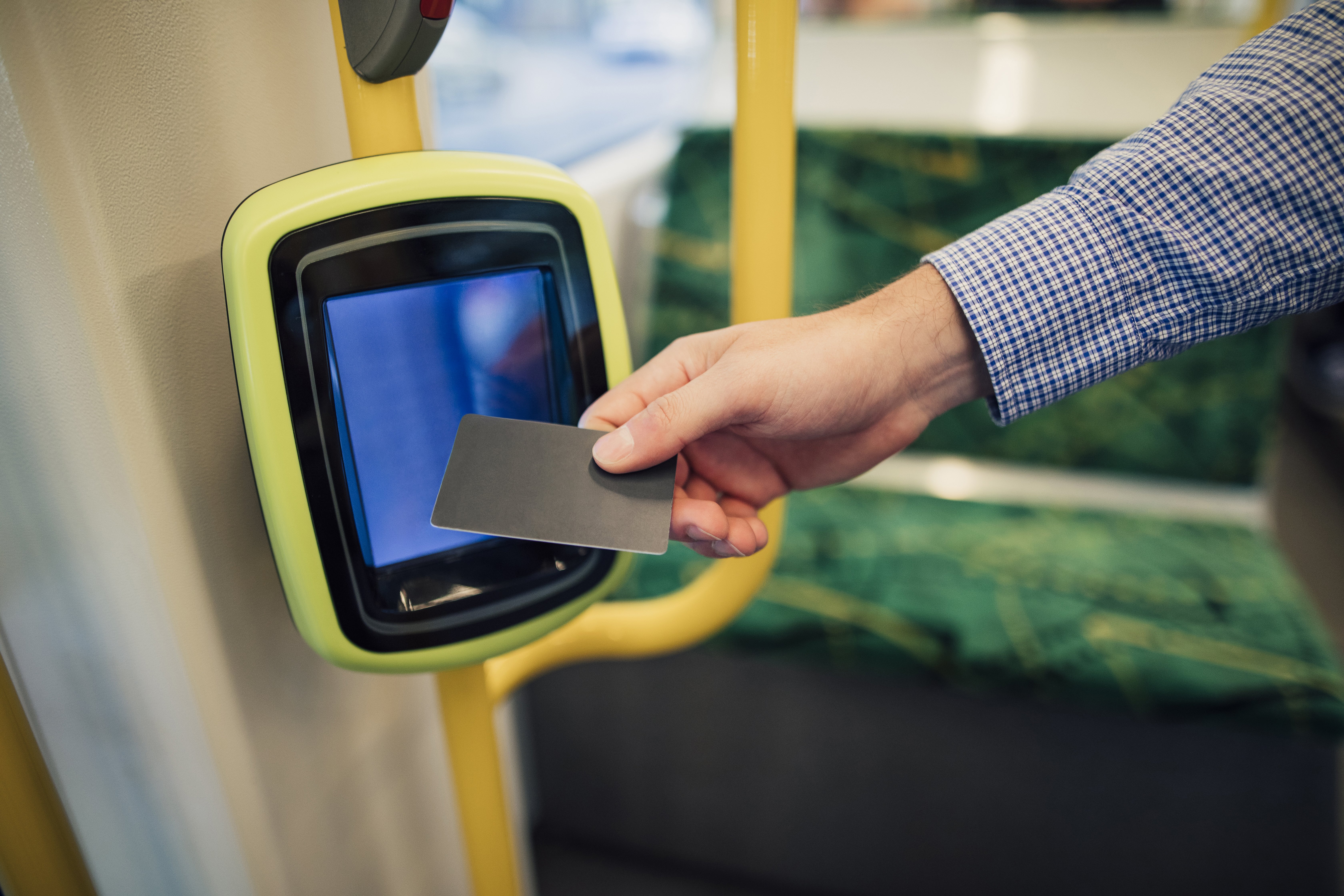 A close-up of a man's hand tapping their public transport card on a card reader. Opting for public transport over your car for a few days a week can help manage costs, especially when it comes to come how much you fill up on petrol every week.