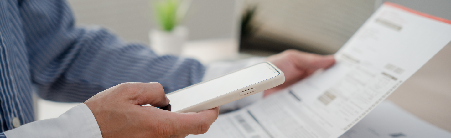 Person holding a mobile phone and a bill