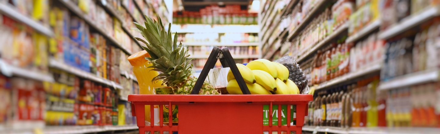 Shopping basket with grocery items in a supermarket aisle.