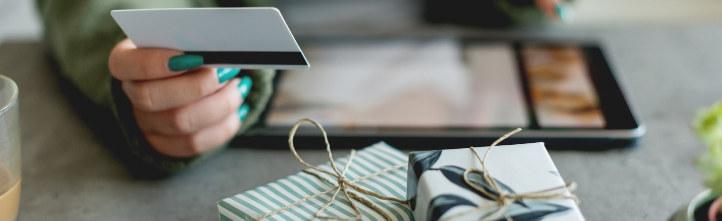 Person with tablet and gifts on table holding a credit card