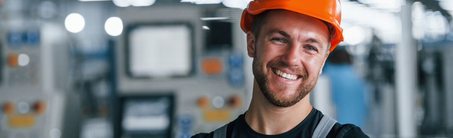 Man wearing a hard hat is smiling while standing in front of heavy machinery. 