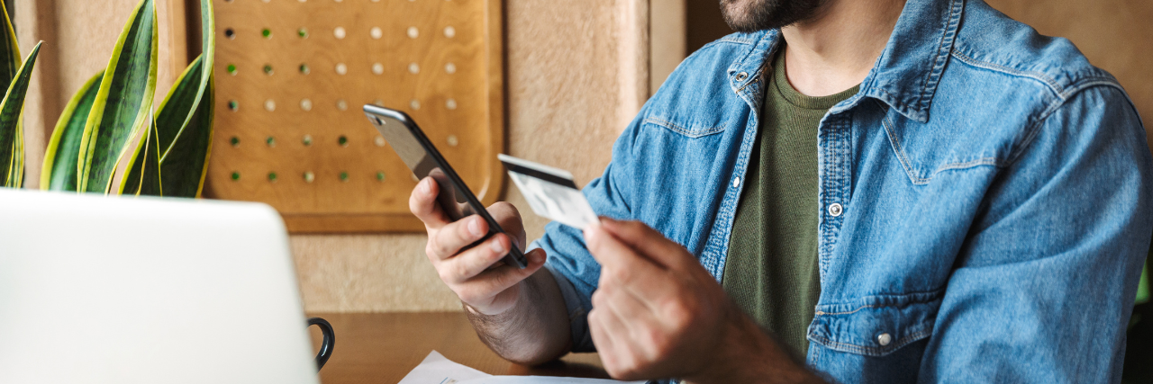 Man holding phone and credit card sitting in front of laptop